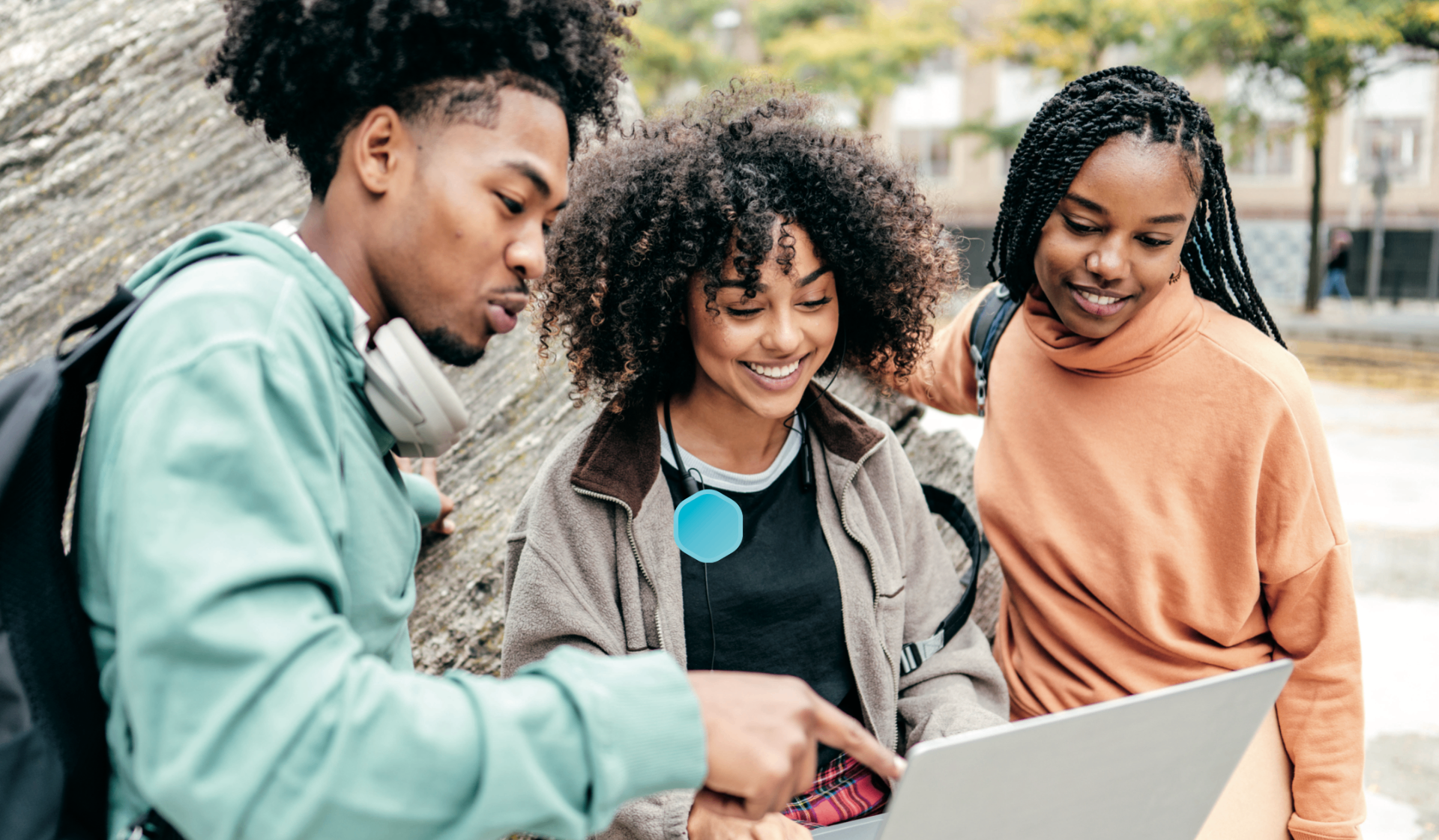 Three university students smiling while looking at a laptop on campus